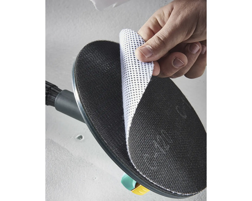 Een hand bevestigt een witte gaasschuurschijf op de zwarte ronde schuurzool van een wandschuurmachine.