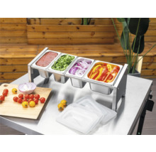 Tenneker Prep Station van roestvrij staal met vier Gastronorm-bakken op een metalen tafel, gevuld met sauzen en gesneden groenten voor het barbecueën.