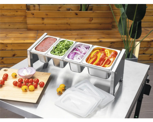 Tenneker Prep Station van roestvrij staal met vier Gastronorm-bakken op een metalen tafel, gevuld met sauzen en gesneden groenten voor het barbecueën.