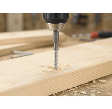 Accuboormachine draait een houtschroef met een bitje in een lichte houten plank, omringd door houtkrullen.