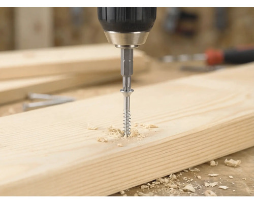 Accuboormachine draait een houtschroef met een bitje in een lichte houten plank, omringd door houtkrullen.