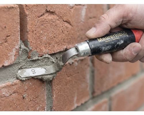 Een persoon gebruikt een Maurerlob voegspijker om mortel tussen rode bakstenen aan te brengen.