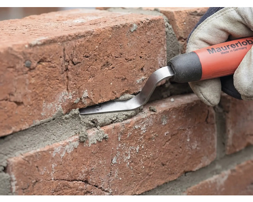 Een voegspijker van Maurerlob wordt gebruikt om mortel in de voeg tussen twee rode bakstenen te drukken.