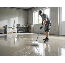 Een man gebruikt een prikroller met telescoopsteel om een vers gegoten vloercoating te ontluchten in een lichte ruimte.