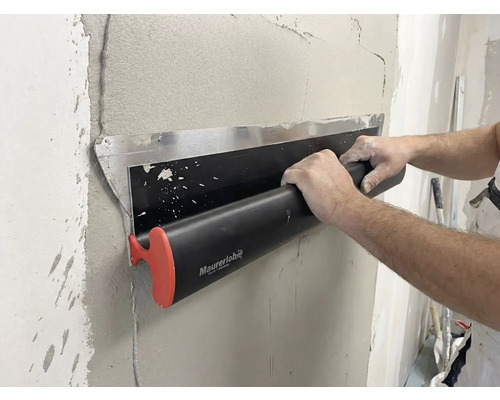 Een persoon gebruikt een Maurerlob-oppervlaktespatel om nat pleisterwerk op een muur glad te strijken.
