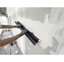 Persoon gebruikt een brede pleisterspaan met roestvrijstalen blad om stucwerk op een muur glad te strijken tijdens renovatie.