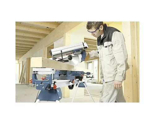 Vakman zaagt een houten balk met een Bosch afkort- en verstekzaag op een werktafel in een lichte bouwomgeving.