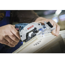 Een persoon snijdt met een Bosch cirkelzaag door een houten plank, met zichtbaar zaagsel.