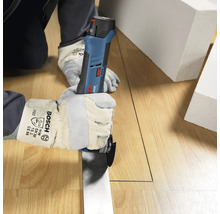 Persoon met werkhandschoenen snijdt met een Bosch Professional accu-multitool een rechte lijn in een houten vloer.