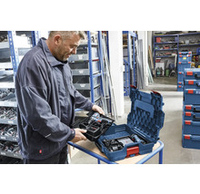 Een man plaatst een inleg met Bosch accuboormachine en lader in een Bosch L-BOXX gereedschapskoffer in een georganiseerde werkplaats.