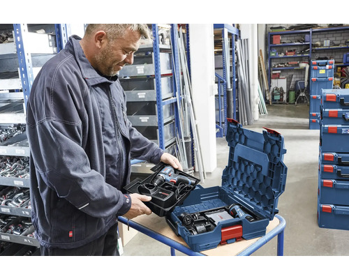 Een man plaatst een inleg met Bosch accuboormachine en lader in een Bosch L-BOXX gereedschapskoffer in een georganiseerde werkplaats.