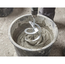 Een spiraalvormige mengstaaf mengt grijze mortel in een zwarte bouwemmer.