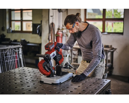 Een persoon gebruikt een accu metaalbandzaag voor het zagen van een metaalprofiel op een werkbank in een werkplaats.