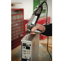 Persoon gebruikt een Dremel 4000 multitool met detailhandgreep voor het graveren van een metalen behuizing in een werkplaats.