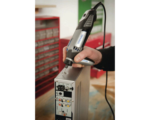 Persoon gebruikt een Dremel 4000 multitool met detailhandgreep voor het graveren van een metalen behuizing in een werkplaats.