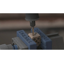 Dremel rotatiegereedschap boort gaten in een houten dobbelsteen die is vastgeklemd in een Dremel bankschroef.