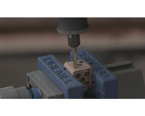 Dremel rotatiegereedschap boort gaten in een houten dobbelsteen die is vastgeklemd in een Dremel bankschroef.
