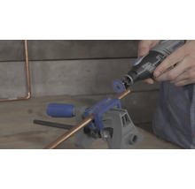 Een koperen buis in een bankschroef wordt gesneden met een Dremel multifunctioneel gereedschap en een doorslijpschijf.