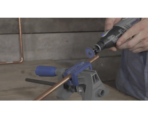 Een koperen buis in een bankschroef wordt gesneden met een Dremel multifunctioneel gereedschap en een doorslijpschijf.