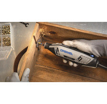 Dremel 4250 multitool snijdt een schroef door in een houten kist met rondvliegende vonken.