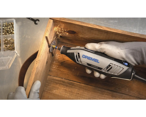 Dremel 4250 multitool snijdt een schroef door in een houten kist met rondvliegende vonken.