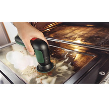 Een hand maakt de glasplaat van een ovendeur schoon met een elektrische accureinigingsborstel en reinigingsschuim.