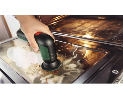 Een hand maakt de glasplaat van een ovendeur schoon met een elektrische accureinigingsborstel en reinigingsschuim.