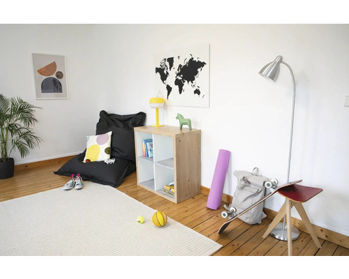 Lichte kamer met houten vloer, houten vakkenkast, zwarte zitzak, zilveren vloerlamp en licht tapijt.