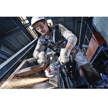 Vakman in beschermende kleding bewerkt een staalconstructie met een accu-haakse slijper met openspattende vonken.
