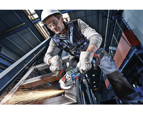 Vakman in beschermende kleding bewerkt een staalconstructie met een accu-haakse slijper met openspattende vonken.