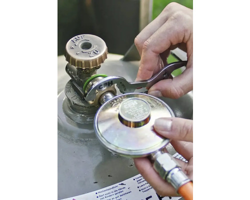 Een persoon sluit een gasdrukregelaar aan op het ventiel van een gasfles met behulp van een CFH gassleutel.