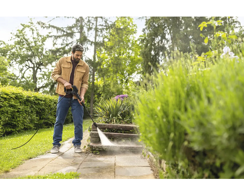 Een man reinigt stenen treden in de tuin met een hogedrukreiniger in een heldere omgeving.