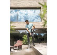 Een man reinigt een licht stenen terras voor een modern huis met een hogedrukreiniger.