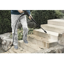 Persoon reinigt een stenen buitentrap met een hogedrukreiniger om vuil en bladeren te verwijderen.
