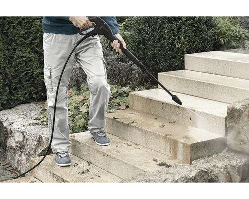 Persoon reinigt een stenen buitentrap met een hogedrukreiniger om vuil en bladeren te verwijderen.