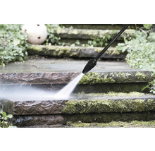 Een hogedrukreiniger reinigt met mos bedekte stenen treden in de tuin met een krachtige waterstraal.