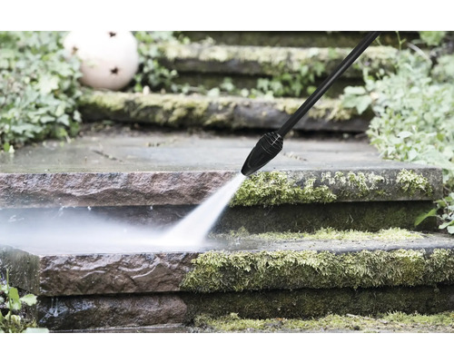 Een hogedrukreiniger reinigt met mos bedekte stenen treden in de tuin met een krachtige waterstraal.
