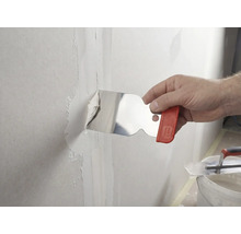 Een hand brengt met een roestvrijstalen plamuurmes plamuur aan op een wandvoeg.
