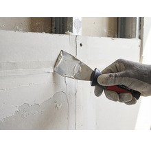 Hand met werkhandschoen brengt met een Rautner plamuurmes vulmiddel aan op een voegband op een gipsplaten wand.