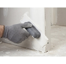 Hand met handschoen brengt vulmiddel aan op een gipsplaat met een applicator.
