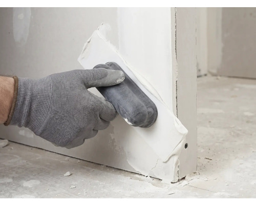 Hand met handschoen brengt vulmiddel aan op een gipsplaat met een applicator.