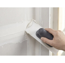 Hand brengt witte plamuur aan op een muur met een plamuurmes.