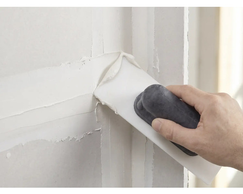 Hand brengt witte plamuur aan op een muur met een plamuurmes.