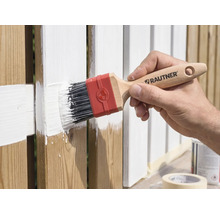 Hand schildert een houten hek met een Rautner platte kwast en witte verf.