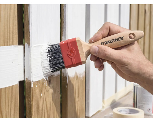 Hand schildert een houten hek met een Rautner platte kwast en witte verf.