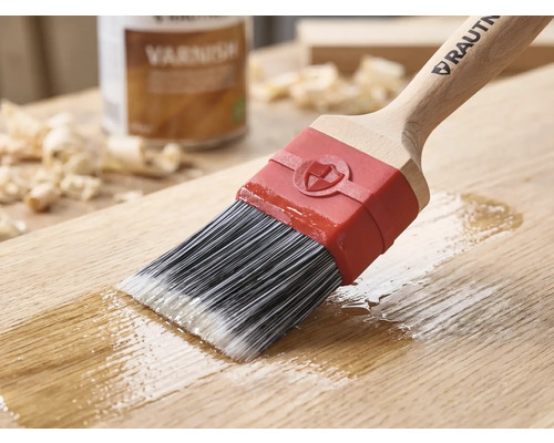 RAUTNER kwast brengt blanke lak aan op een houten oppervlak. Met synthetische haren, houten handvat en rode huls. Op de achtergrond een blik lak.