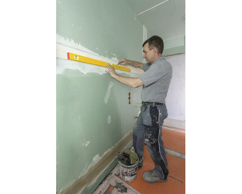 Vakman gebruikt een waterpas en een potlood om een horizontale lijn te markeren op een groene gipsplaten wand.