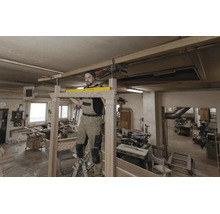Vakman in een werkplaats gebruikt een waterpas om een houten frame uit te lijnen terwijl hij op een ladder staat.