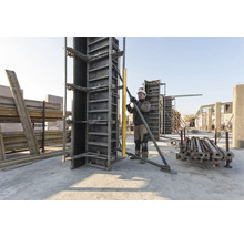 Bouwvakker lijnt een verticale betonbekisting uit op een lichte bouwplaats met een waterpas en een metalen schoor.
