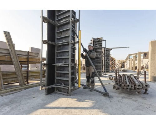 Bouwvakker lijnt een verticale betonbekisting uit op een lichte bouwplaats met een waterpas en een metalen schoor.